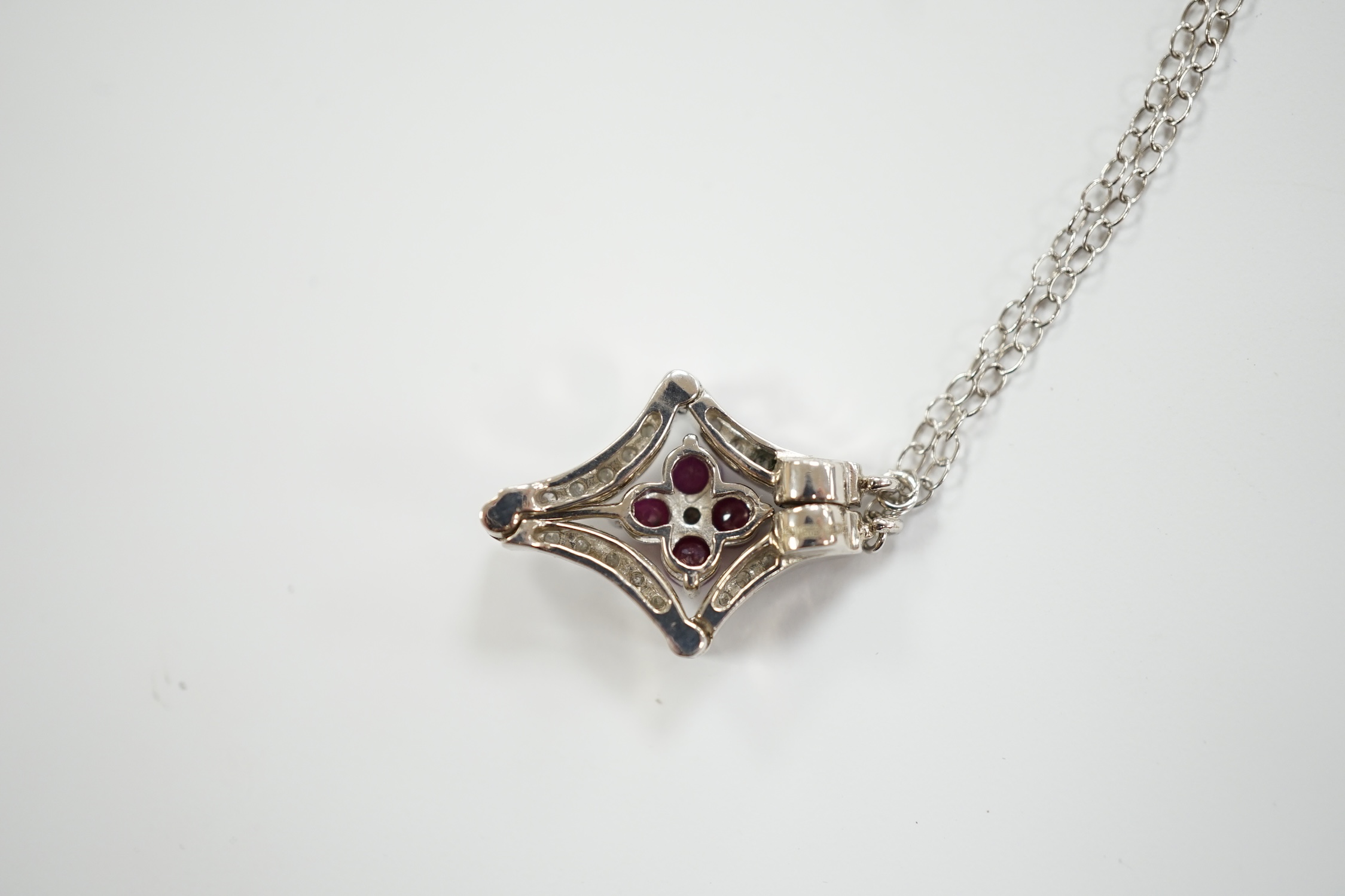 A modern 14ct white gold, ruby and diamond cluster set metamorphic pendant, 21mm, on a 14k white metal fine link chain, 38cm, gross weight 3.8 grams.
